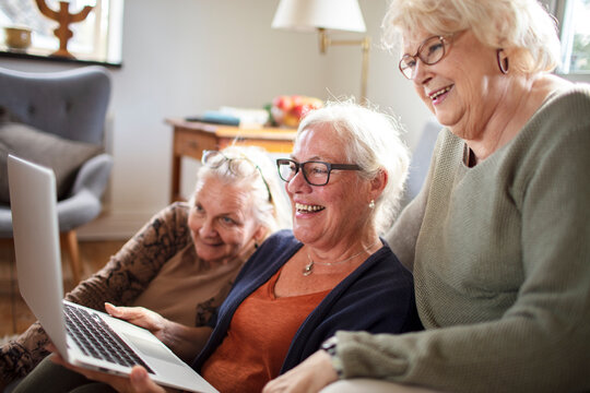 Senior women friends using laptop at home