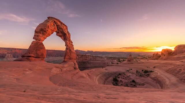 Sunrise lights up Delicate Arch sandstone landscape with golden sky motion.