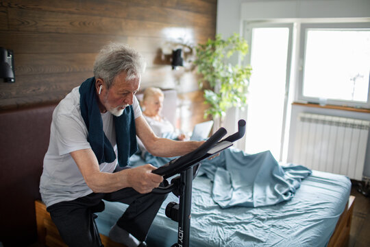 Senior man exercising on stationary bike in bedroom at home