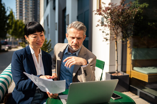 Two business colleagues reviewing documents on laptop at an outdoor cafe in the city