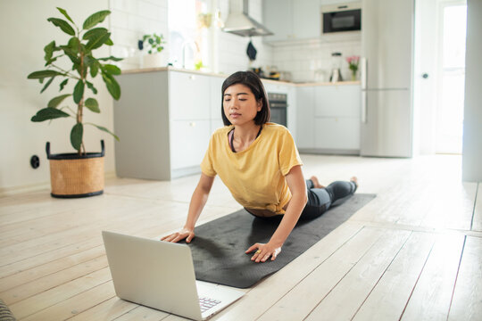 Young woman practicing yoga with laptop at home kitchen