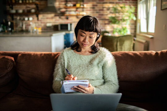 Woman writing notes while working from home on sofa
