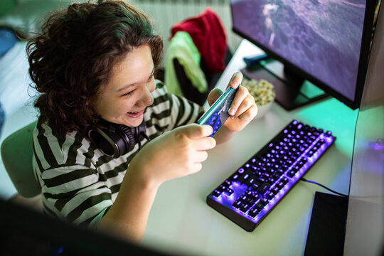 Smiling teenager playing mobile game at home gaming setup