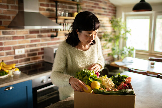 Woman unpacking fresh produce delivery at home kitchen