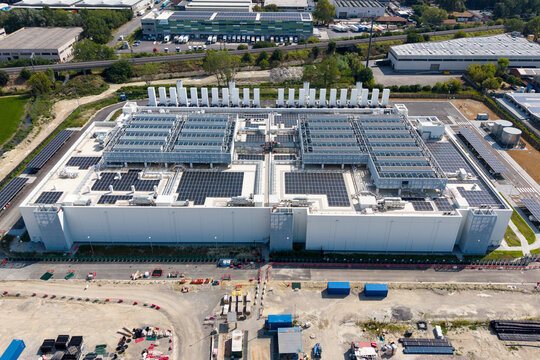 Aerial view of a large hyperscale data center campus featuring extensive rooftop solar panels and cooling infrastructure under construction in Melegnano, Lombardy, Italy.
