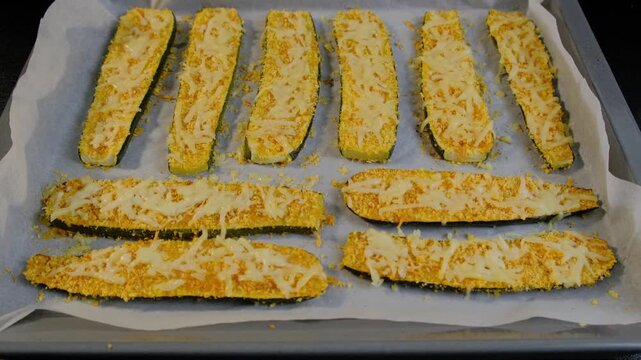 Hands arrange breaded zucchini slices on a baking sheet, topped with cheese, in a Cooking kitchen setting.