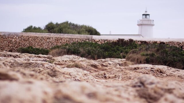 White lighthouse rising behind dry stone wall on rocky coast