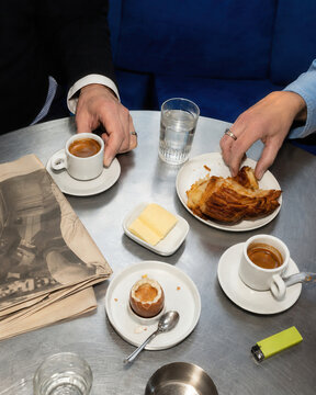 Hands reaching espresso and croissant breakfast arranged on a cafe table
