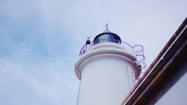 Low angle view of white lighthouse lantern against blue cloudy sky