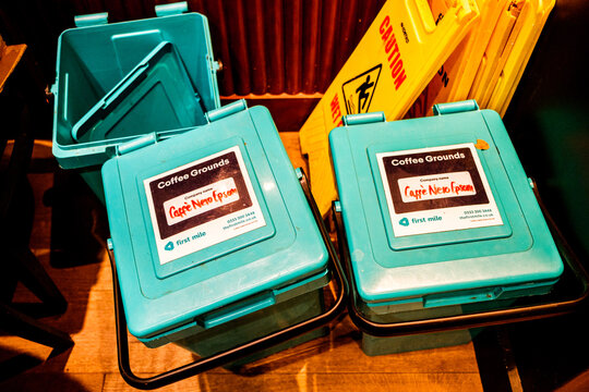 A Close-Up Shot of Used Coffee Grounds Collection Bins And Yellow Wet Floor Warning Signs Inside A Caffe Nero Coffee Shop Store, With No People Visable