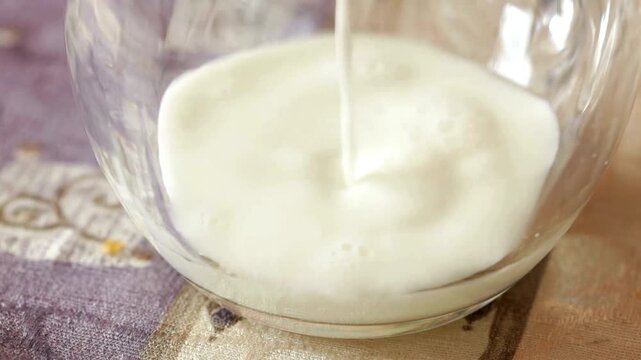 Fresh milk pouring into glass bowl, creamy white liquid splashing in slow motion, dairy product preparation for cooking and baking