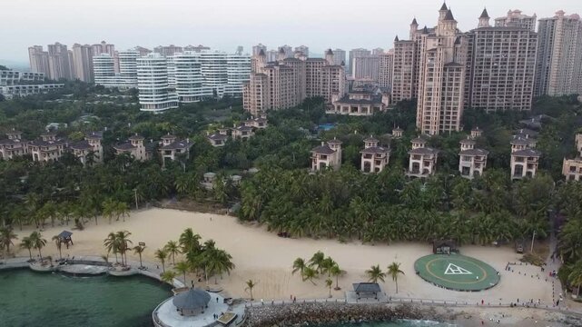 Aerial view of Sanya Beach and ocean with palm trees, resort buildings, and a helipad in Sanya, Hainan, China.