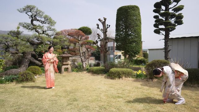 Two women in traditional kimonos stroll a peaceful garden. One wears soft peach, the other muted cream. Their steps echo gentle movement through trimmed hedges