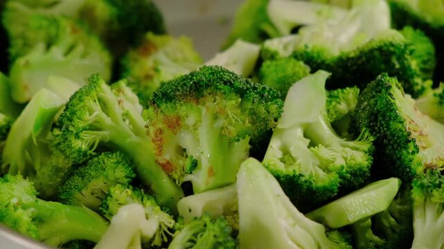 Close-up of cooked broccoli florets and stalks in a bowl, with light browning from roasting, at Cooking location during daytime.