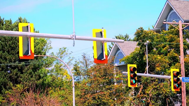 Urban Traffic Lights Hanging from Horizontal Mast Arm Against Houses and Trees