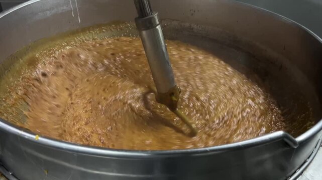 Caramel sauce being continuously mixed in an industrial steam-heated kettle during food manufacturing operations. Large-scale cooking process supporting product consistency, texture control, and comme