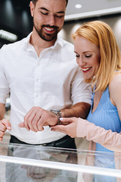 Happy man and woman examining a sophisticated wristwatch inside a bright retail jewelry store, making a special purchase together.