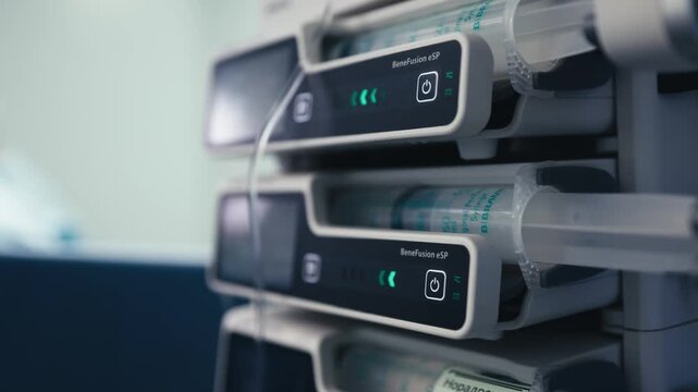 Multiple medical infusion pumps are installed beside the operating table while a surgical team performs an operation in the background.