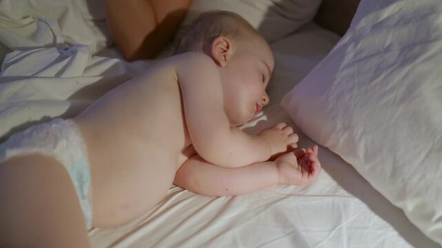 Infant child peacefully sleeping on a bed with white sheets and pillows, showing gradual changes in position and posture across the frames