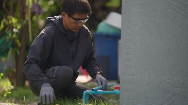 Professional plumber fixes a residential water pipeline connection outdoors, showing pipe repair, plumbing maintenance, valve servicing, household utilities, and property upkeep.