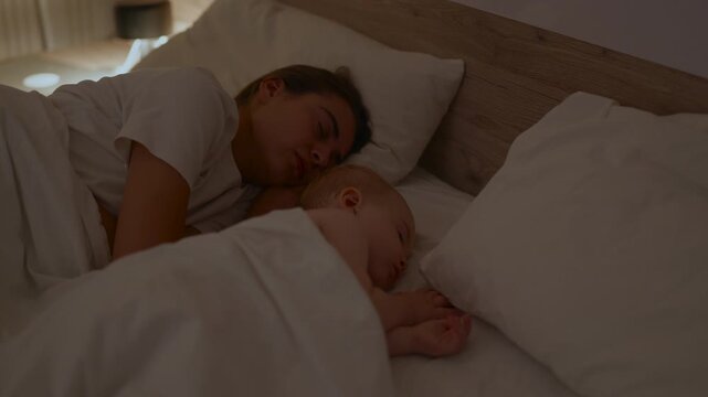 Mother and infant peacefully sleeping together in a cozy bedroom, wrapped in white blankets, soft lighting creating a serene atmosphere for rest and relaxation
