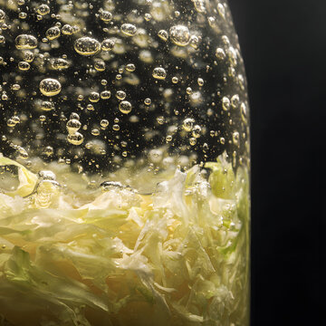 Shredded cabbage submerged in bubbling fermenting liquid showing active lactic fermentation with rising bubbles and pale green layers creating textured, organic, probiotic scene