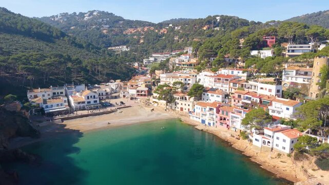 Aerial view of the coastal town of Begur with white buildings nestled along the turquoise bay surrounded by lush hills in Begur, Catalunya, Spain.