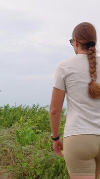 Vertical video. Young Woman Walks Along a Windy Mountain Trail With a Scenic View of the Tropical Sea and Islands, Adventure and Active Travel