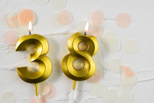 Thirty-eighth anniversary celebration. A golden burning candle in the shape of the number thirty-eight on a festive white background with confetti and glitter. Festive banner.