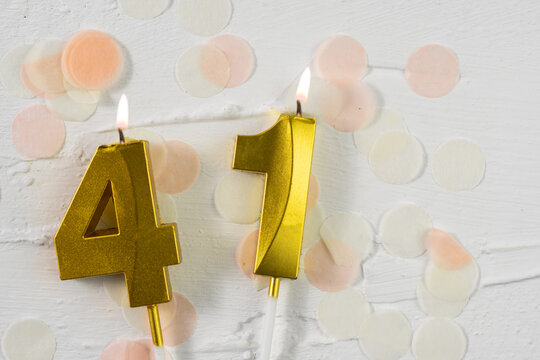Forty-first anniversary celebration. A golden burning candle in the shape of the number forty-one on a festive white background with confetti and glitter. Festive banner.