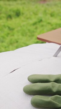Vertical video. Gardener Wearing Protective Gloves Cuts Open a White Soil Bag with a Knife Outdoors, Preparing Potting Material for Container Plant Cultivation