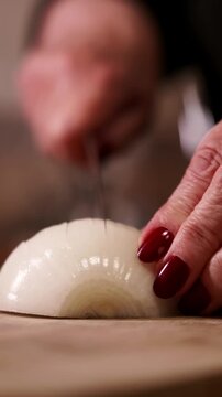 Woman's hands slicing white onion with kitchen knife closeup.