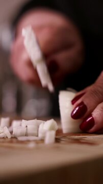Woman's hands slicing white onion with kitchen knife closeup.