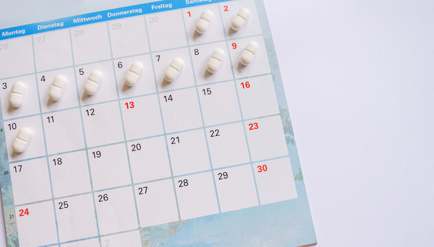 Daily medication schedule concept with white pharmaceutical pills organized on a wall calendar background for tracking healthcare treatment, medical routine compliance, and chronic illness management.