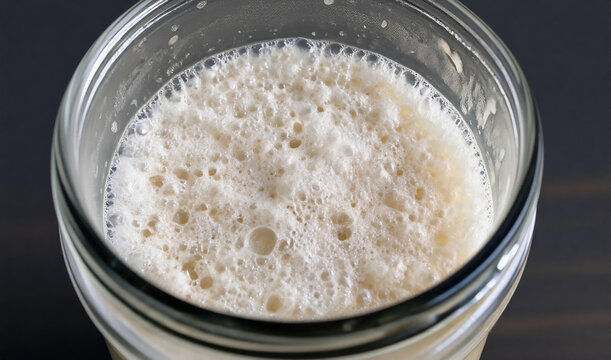 Active bubbling sourdough starter in a glass jar, top view of homemade wild yeast fermentation process for baking bread