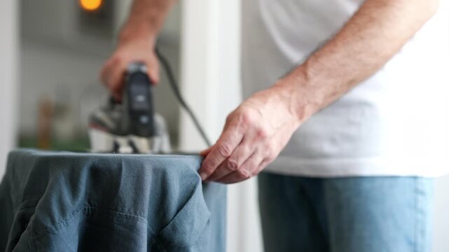 Man ironing a blue shirt on an ironing board at home