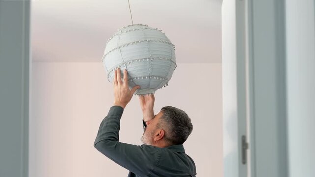 Mature man installing a modern paper lantern in his new apartment