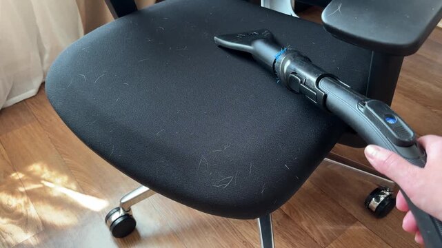 Vacuum cleaner removing pet hair from the fabric surface of a black chair. Concept of house cleaning, pet hair removal, upholstery care and maintaining a clean workspace with pets