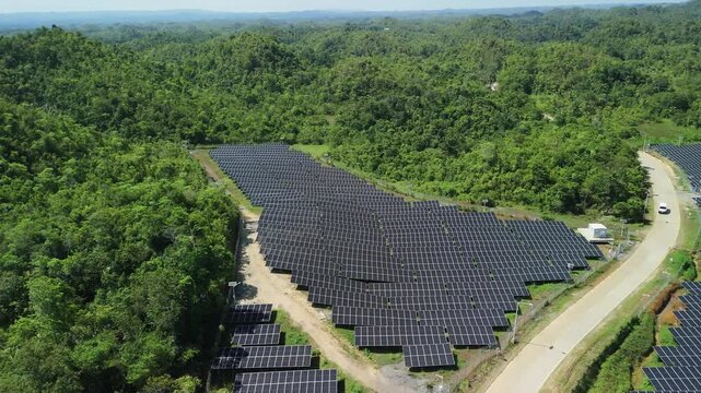 Aerial view of Sikatuna Solar Power Plant with rows of photovoltaic panels surrounded by lush green forest in Sikatuna, Central Visayas, Philippines.