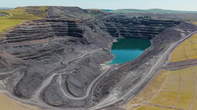 Drone pushing slowly forward over vast open pit mine, showing terraced earth layers and accumulated water from past extraction activities