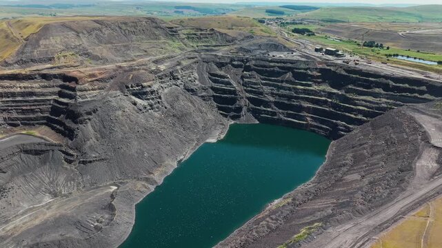 Abandoned opencast coal mine pit at Ffos-y-Fran near Merthyr Tydfil, South Wales, deep water filling dark terraced quarry crater amidst damaged landscape