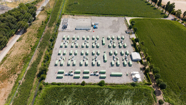 Aerial view of the BESS SERRE TAVAZZANO battery energy storage system with rows of green containers on a gravel lot surrounded by fields in Tavazzano con Villavesco, Lombardy, Italy.