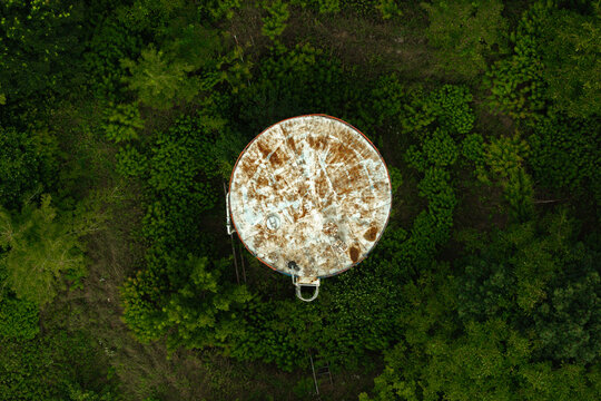 Aerial view of an old rusted fuel storage tank surrounded by dense green forest foliage in Poland.