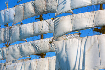 White sails of a tall sailing ship against a clear blue sky. Close-up maritime background with traditional rigging, nautical details and wind-filled canvas. © Serhii