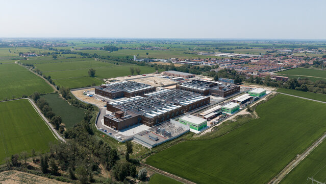 Aerial view of Stack Infrastructure MIL04 Campus featuring modern data center buildings surrounded by lush green fields and agricultural land in Vellezzo Bellini, Lombardy, Italy.