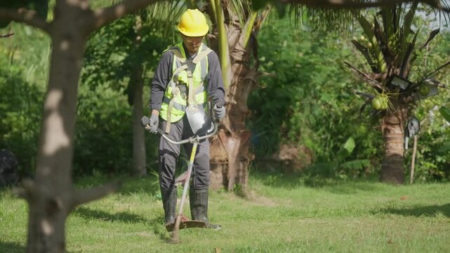 Maintenance worker in protective gear operates a brush cutter on a grassy property, highlighting occupational safety, lawn maintenance, landscaping services and skilled outdoor labor.
