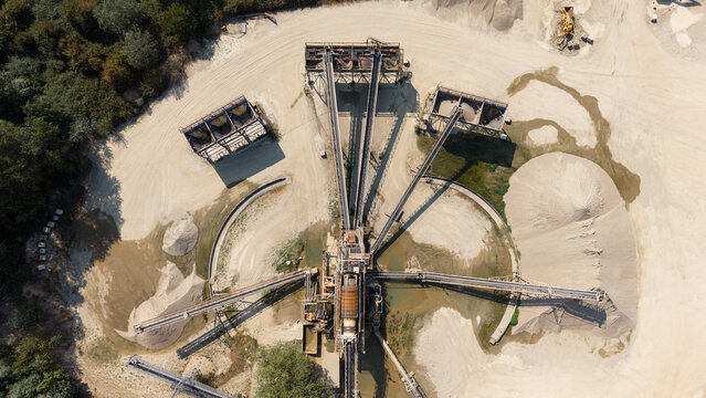 Aerial view of a gravel quarry featuring industrial crushing and screening machinery for aggregate processing, with piles of sand and gravel in Zibido San Giacomo, Lombardia, Italy.