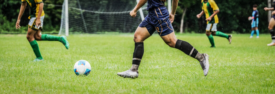 Soccer player running with ball during competitive football match on outdoor grass field