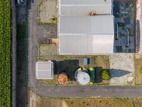 Aerial view of an industrial facility featuring a large warehouse, storage tanks, and paved access roads in Chivasso, Piedmont, Italy.