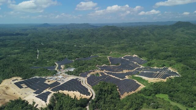 Aerial view of the Sikatuna Solar Power Plant with rows of solar panels situated among lush green hills in Sikatuna, Central Visayas, Philippines.